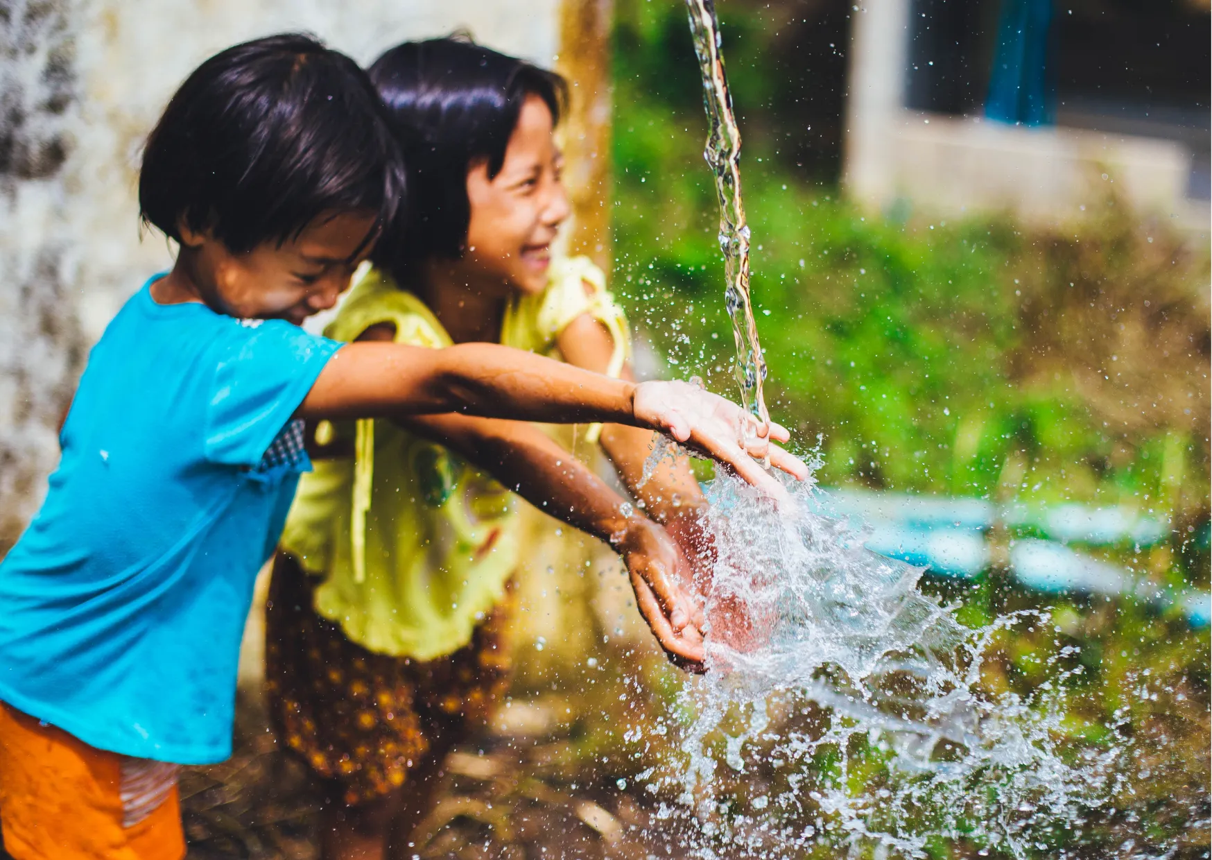 Sauberes Wasser verändert Leben – Projekt Welthungerhilfe Zwei Kinder spielen lachend mit fließendem Wasser aus einem Brunnen
