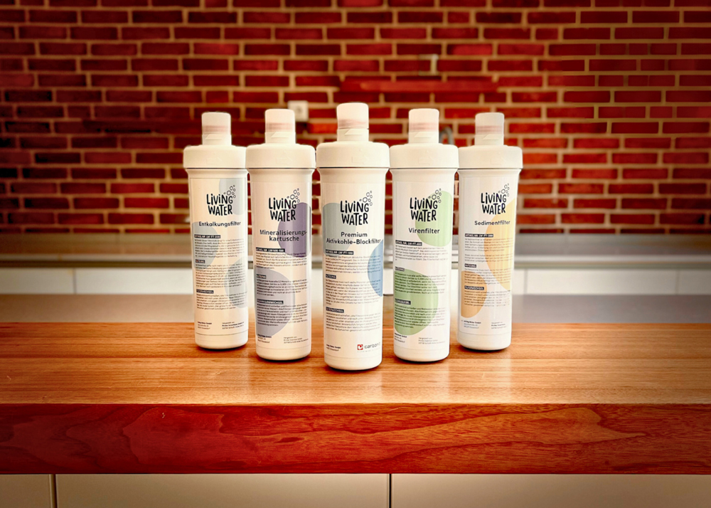 Fünf Wasserfilterflaschen auf einer Holzoberfläche vor einer gemauerten Wand.