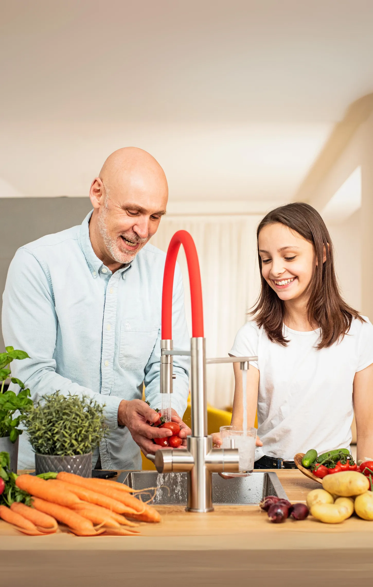 Ein Mann und ein Mädchen stehen am Küchenwaschbecken und waschen Gemüse, darunter Tomaten und Karotten.