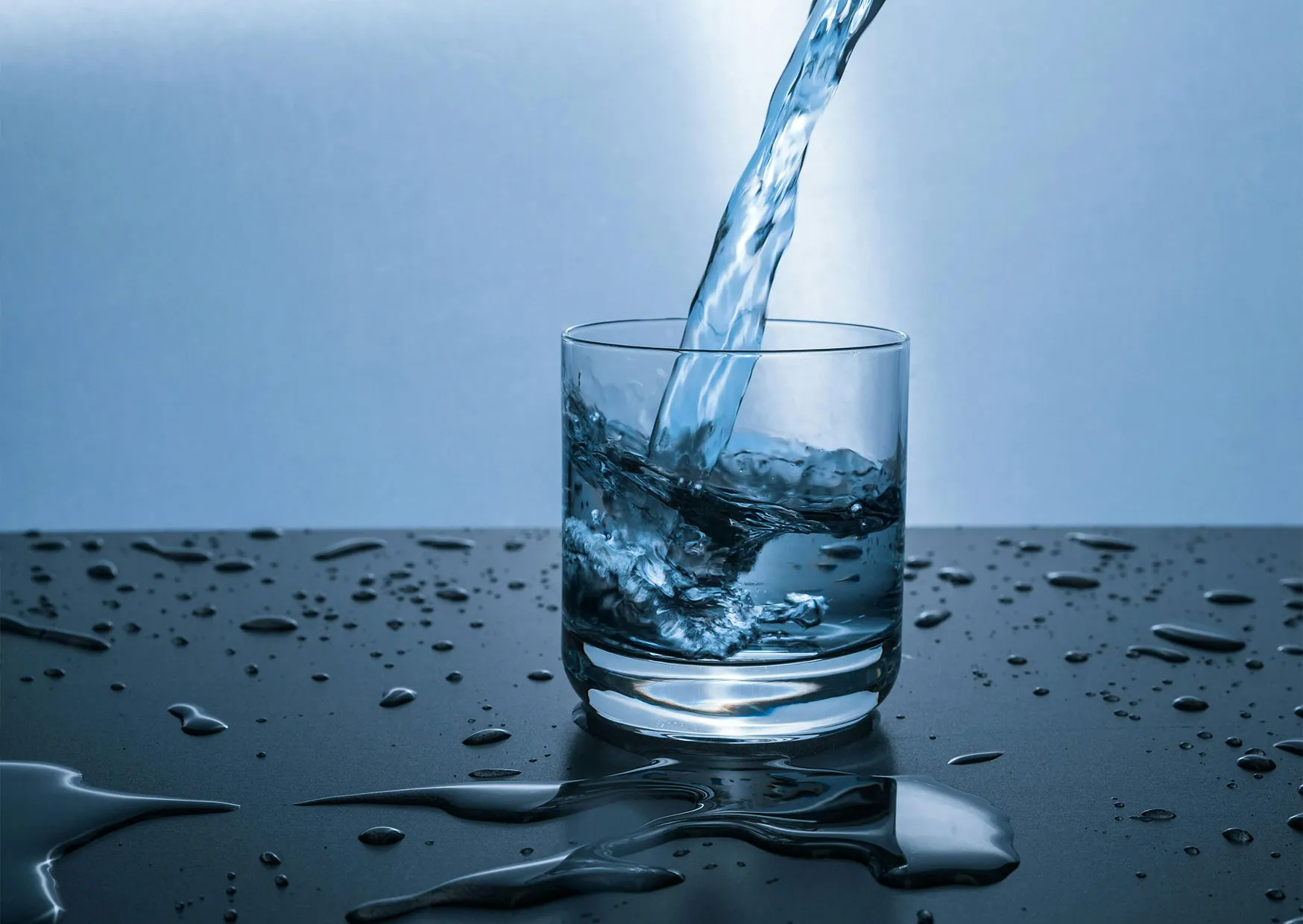 Klares Wasser nach der Filtration Ein Glas wird mit Wasser gefüllt, während Wassertropfen auf einer Oberfläche spritzen.