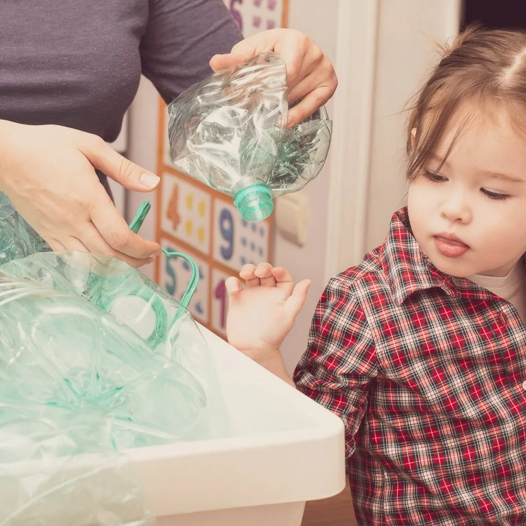 Gemeinsam Plastikmüll reduzieren und Verantwortung übernehmen Kind und Erwachsene sortieren gemeinsam leere Plastikflaschen in einem weißen Behälter.