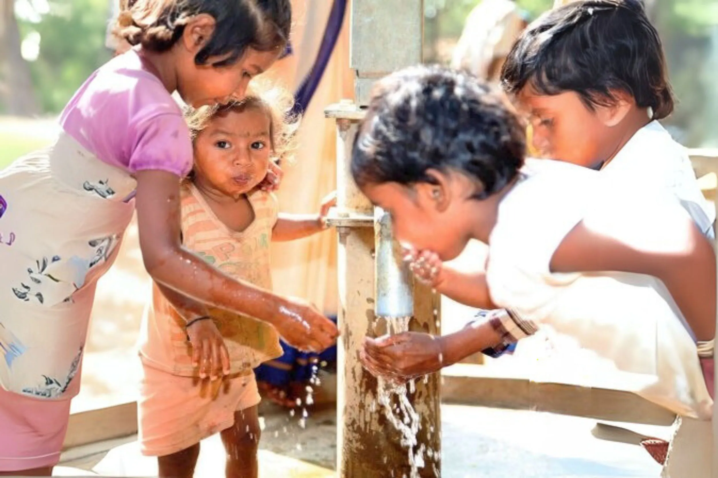 Vier Kinder, die an einer Wasserpumpe spielen und sich mit Wasser bespritzen.