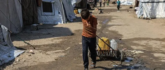 Ein Junge zieht einen selbstgebauten Wagen mit Kanistern durch ein Flüchtlingslager in Gaza.