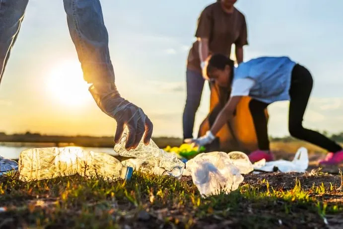 Menschen sammeln Plastikflaschen und weiteren Müll am Ufer.